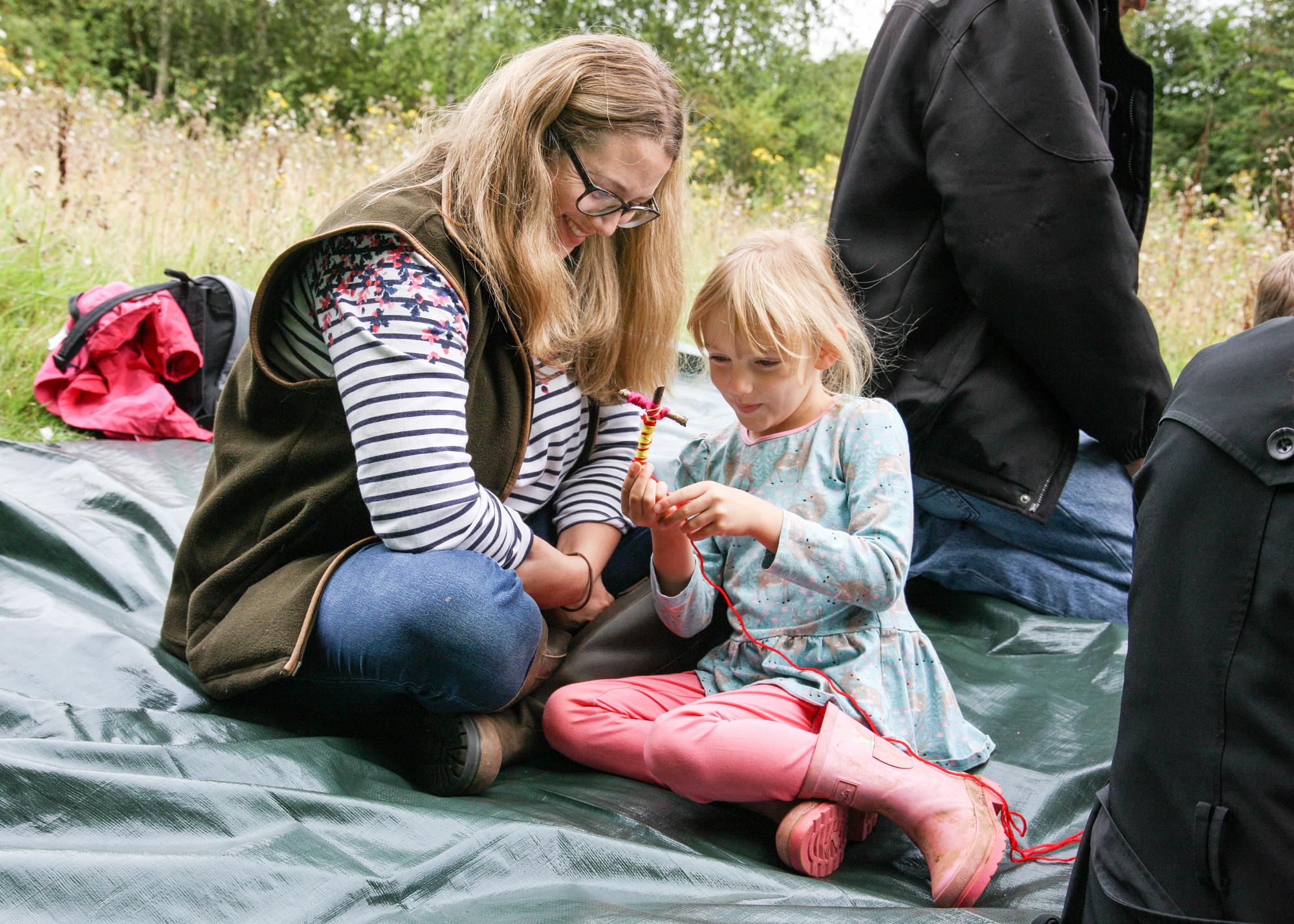 Mum sitting with daughter making a stickman in the Forest 