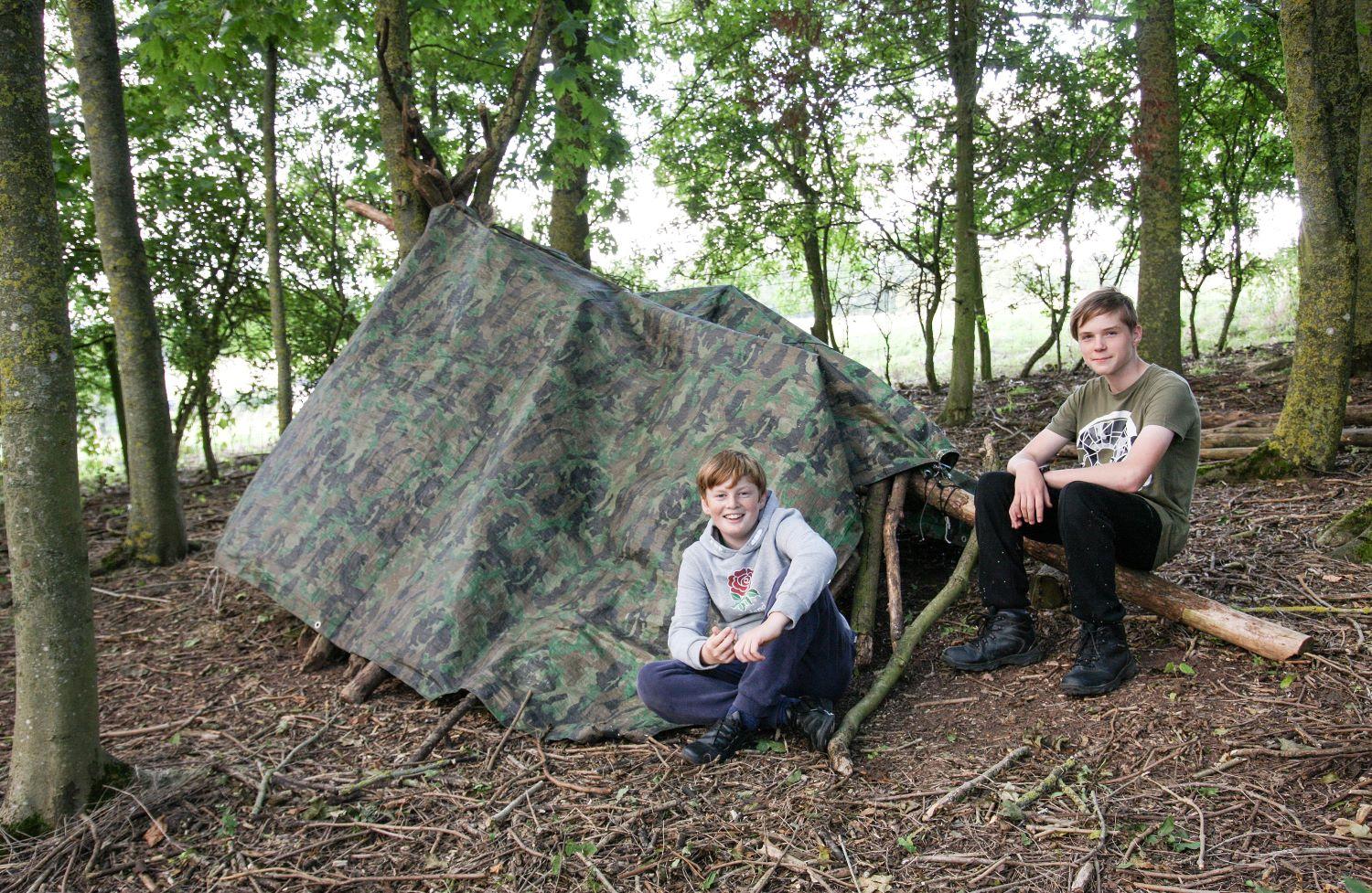 2 young Foresters with a tent they've built in the Forest