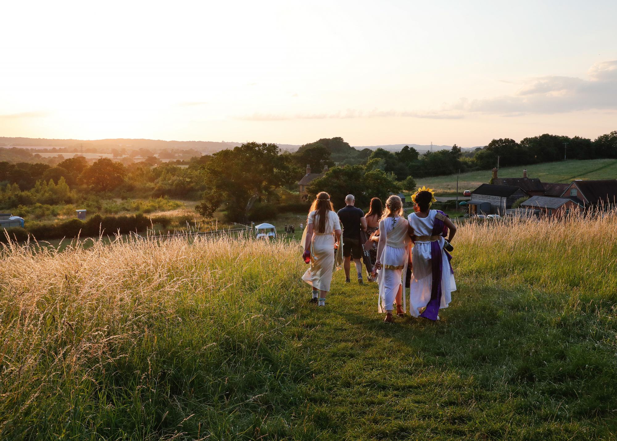 The school children in costume walking off into the sunset along a mowed path in long grass with the sun setting