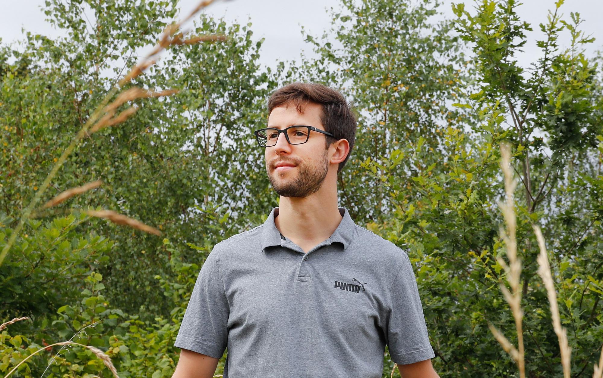 Alexander wearing glasses looking off to the left, surrounded by trees and grassland