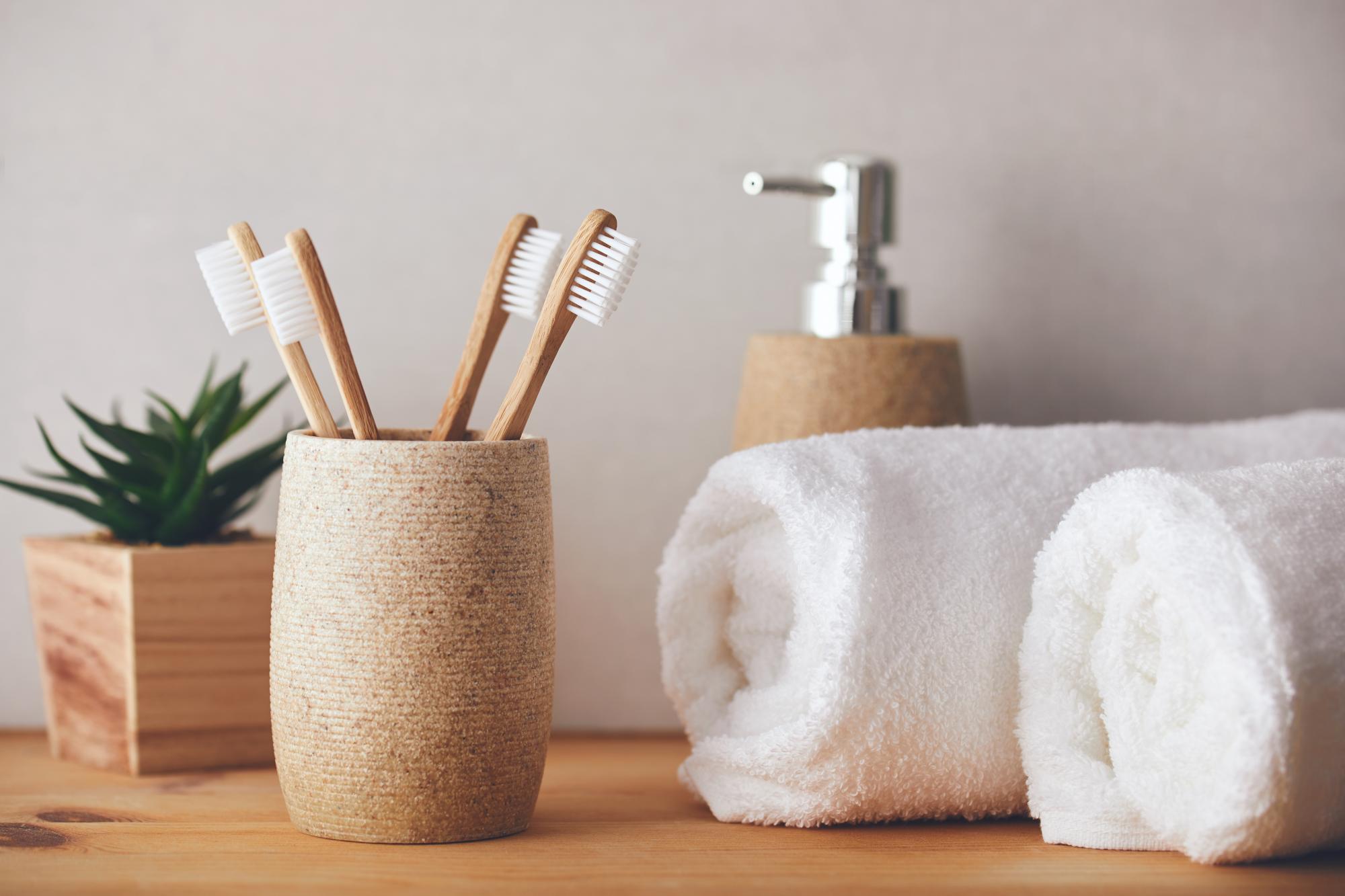 Four bamboo toothbrushes in a wooden toothbrush holder on left. Soap dispenser and two small, white towels on right.