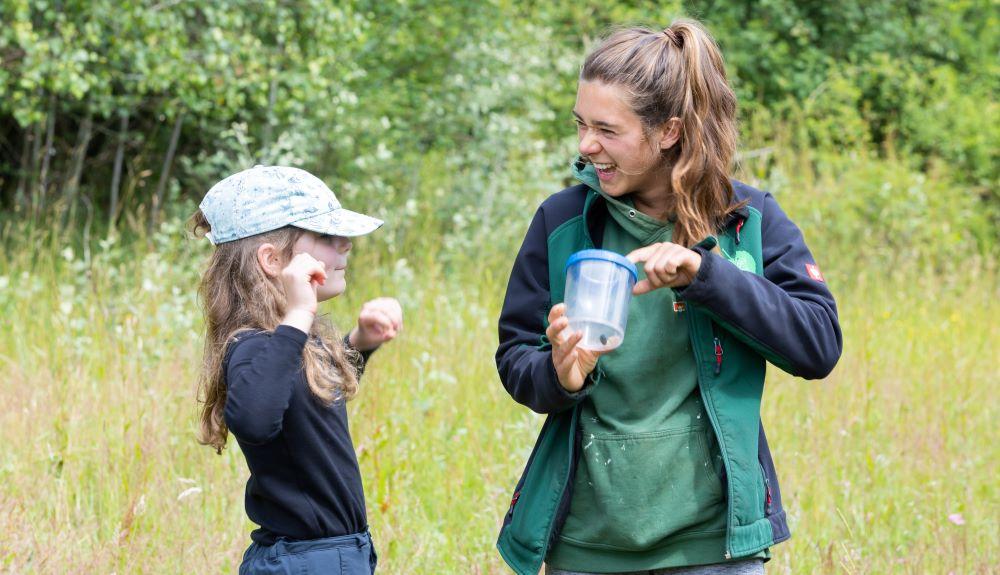 Forest Ranger Phoebe holding a bug jar and laughing with a young girl out in the Forest 