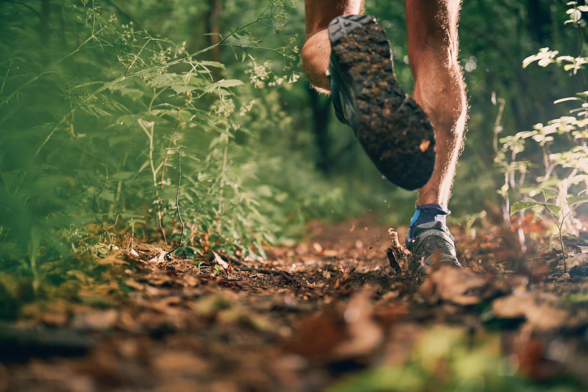 The feet of a running man on a path covered in fallen autumnal leaves