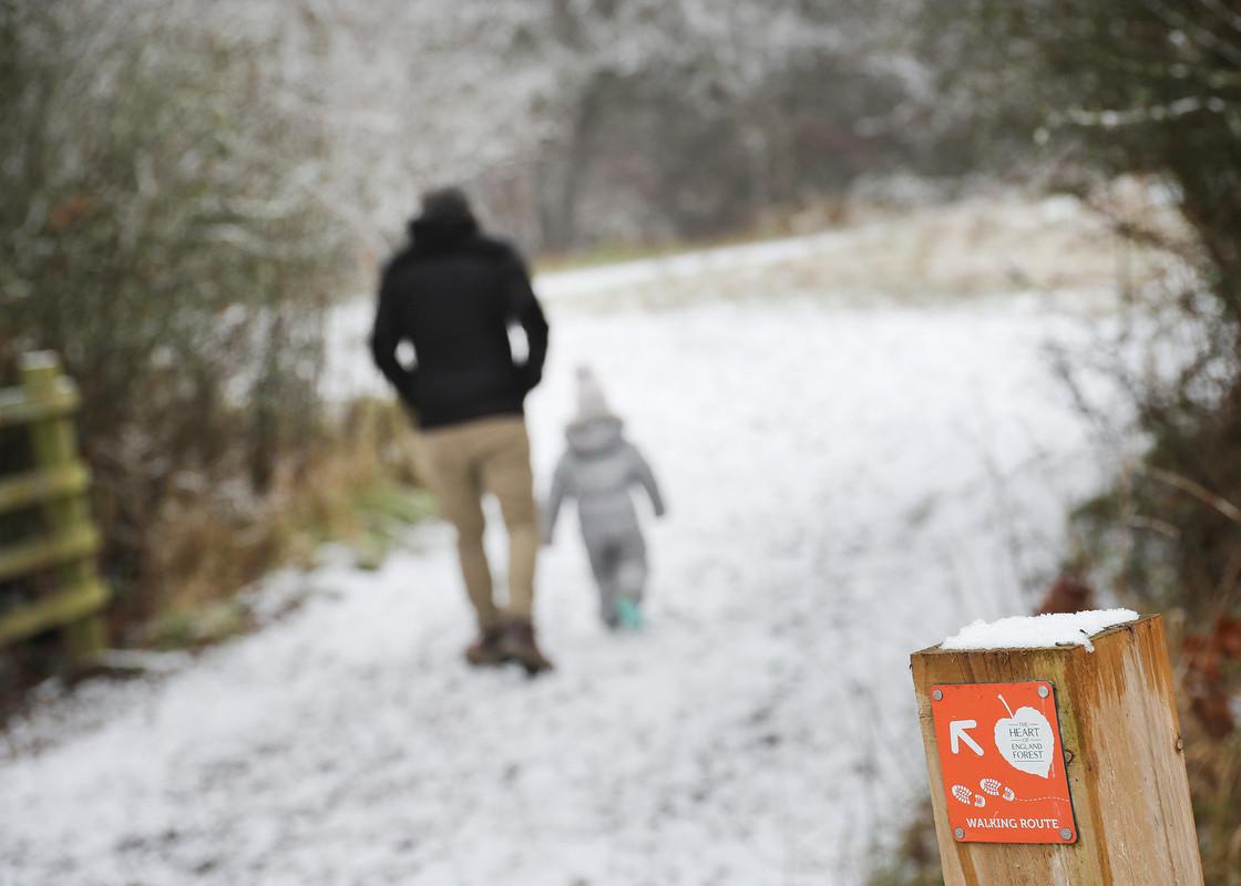 A man and young child walking away down a snowy footpath in the Forest with a footpath marker in the foreground