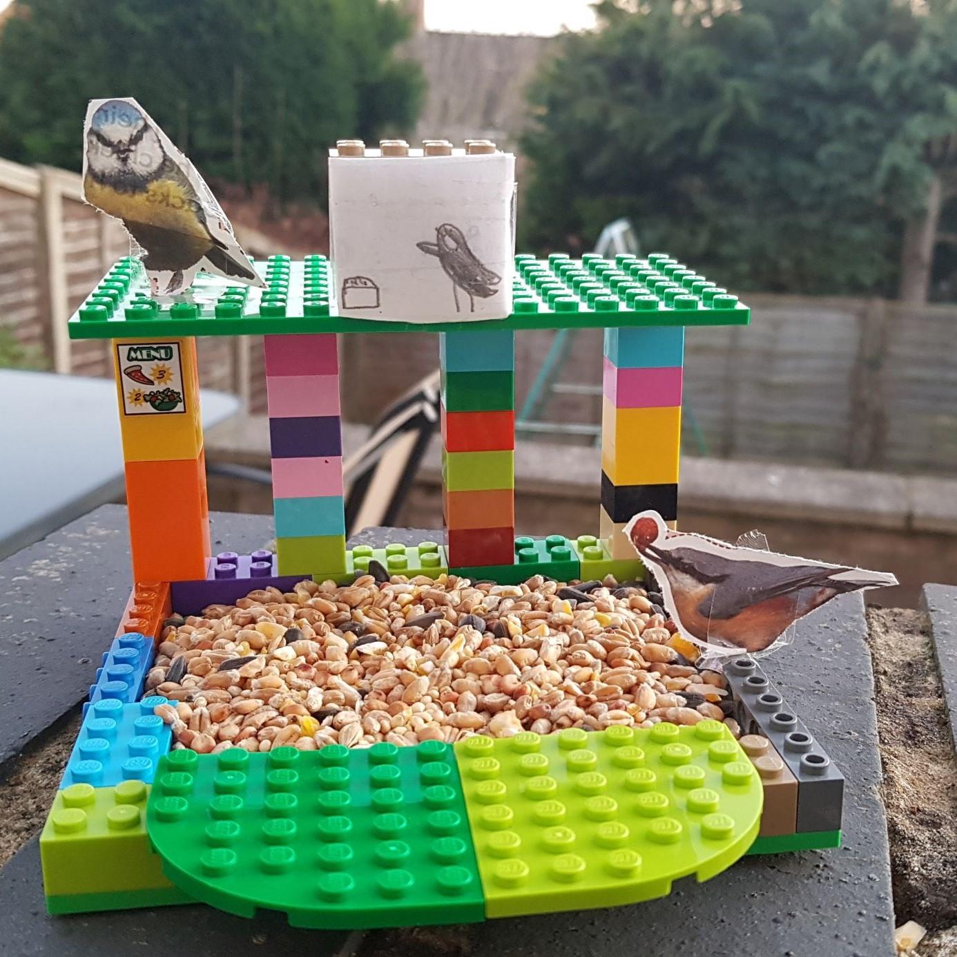 Brightly coloured bird feeder made out of lego, with the base filled with bird seed