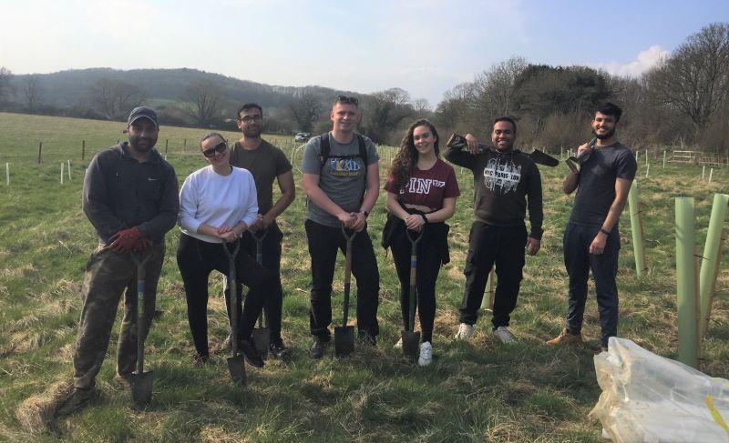 A group of seven young people standing with spades in a tree planting field