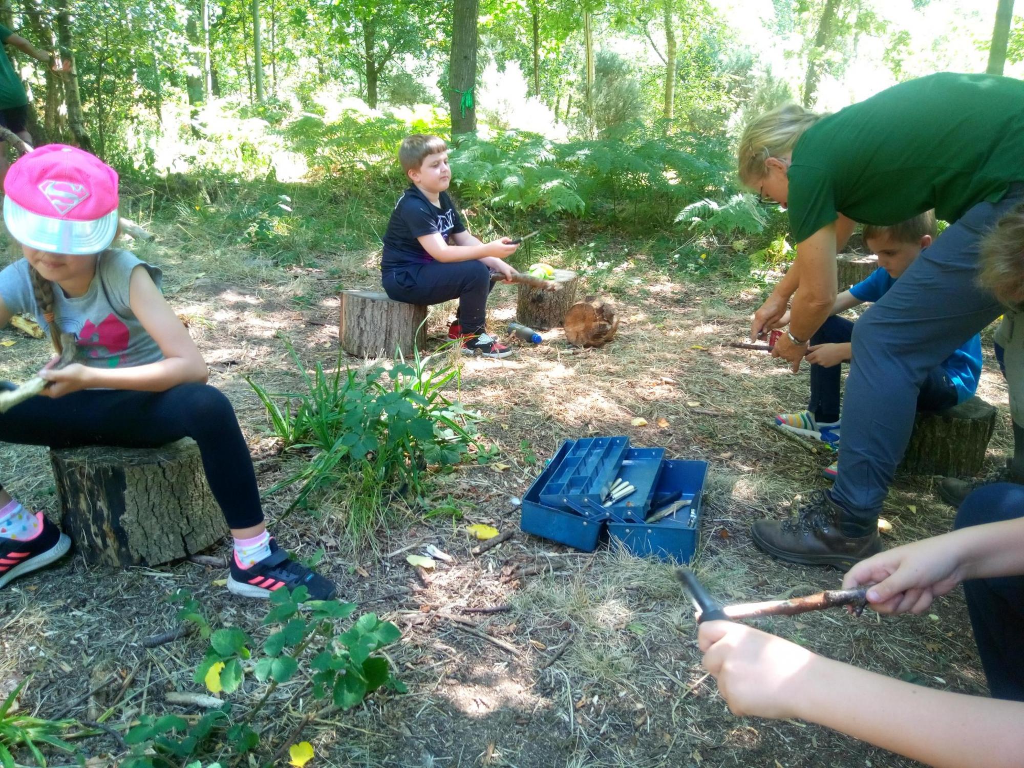 Children sitting on stumps in the woodland whittling