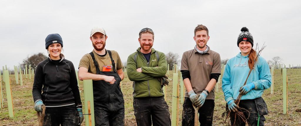 Five members of our forestry team standing together in a tree planting field smiling at the camera