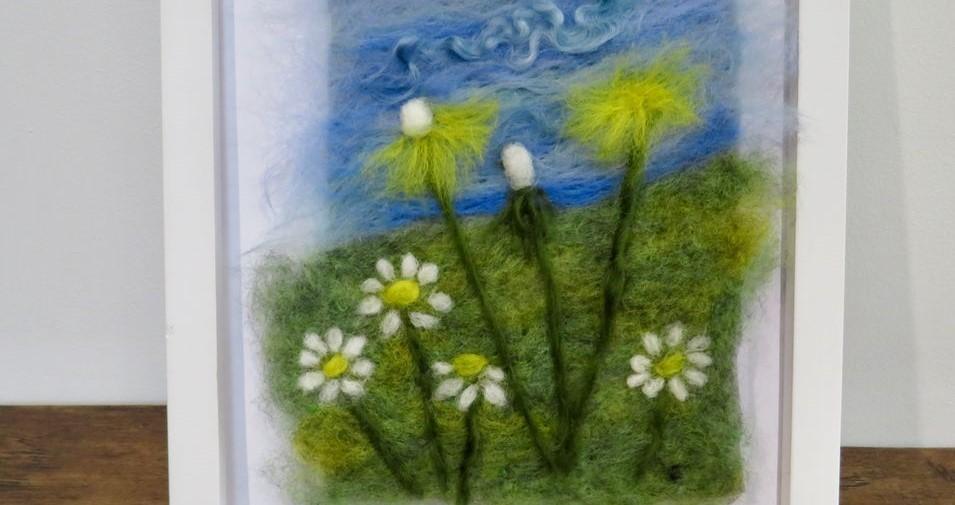 An framed felted image of flowers, grass and blue skies