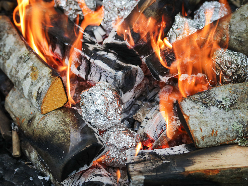 A close-up of a campfire with potatoes wrapped in tinfoil cooking over it