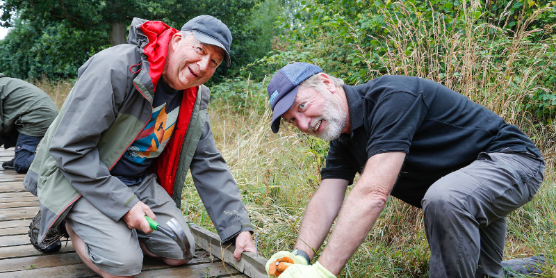 Two male volunteers smiling fixing a board walk in morgrove coppice