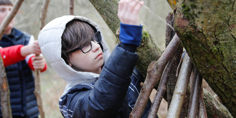 A young child building a den in the Forest using sticks and string.