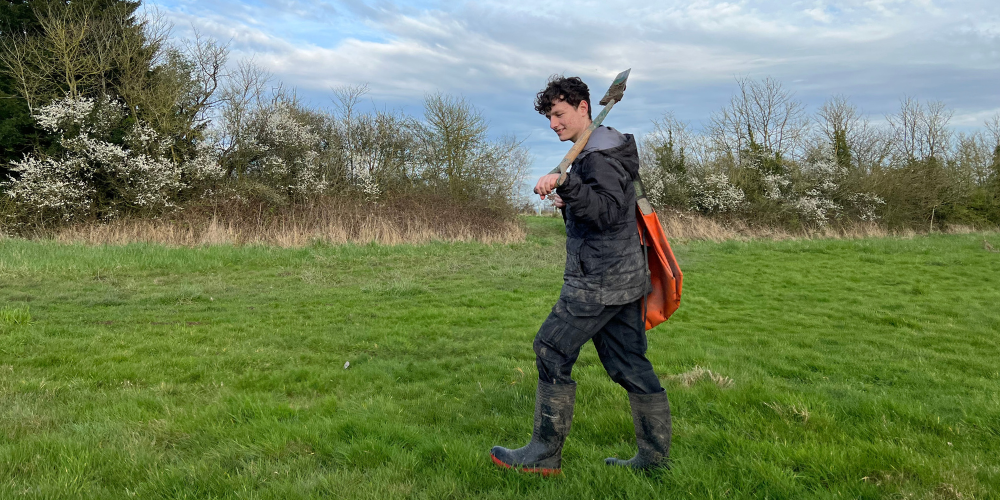 Harrison walking through a field with a tree planting bag and spade in hand