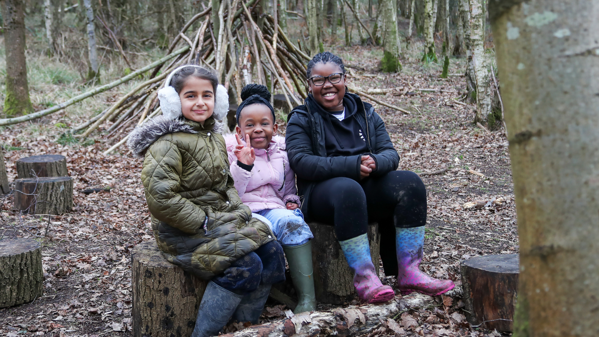 Three students sitting on logs in our outside classroom