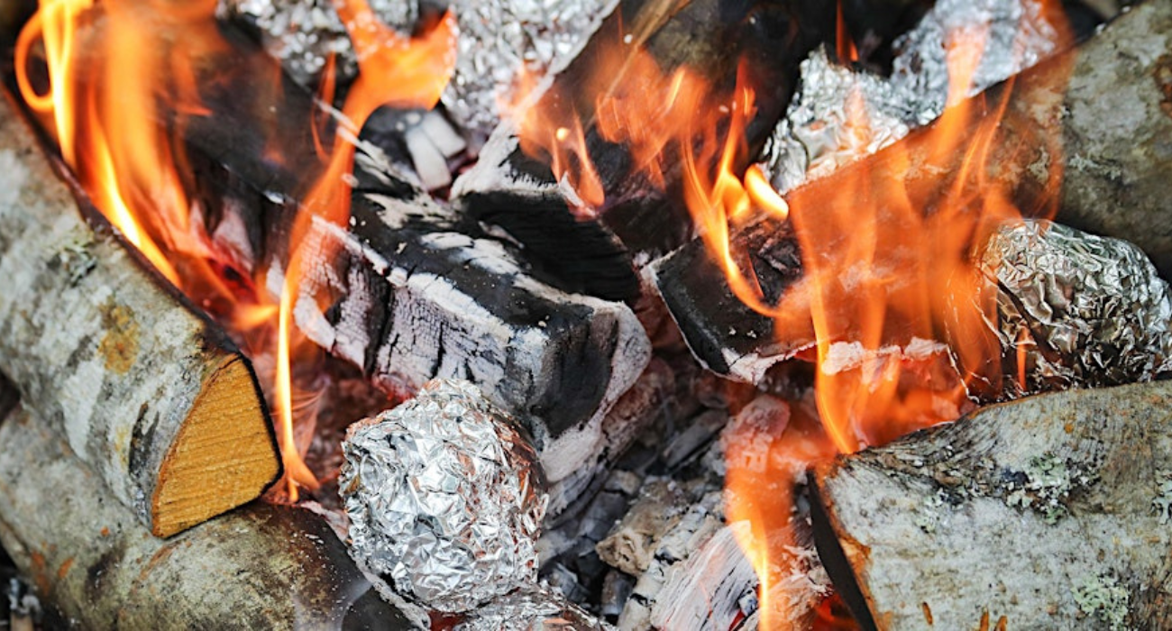 A close-up of a campfire with potatoes wrapped in tinfoil cooking over it
