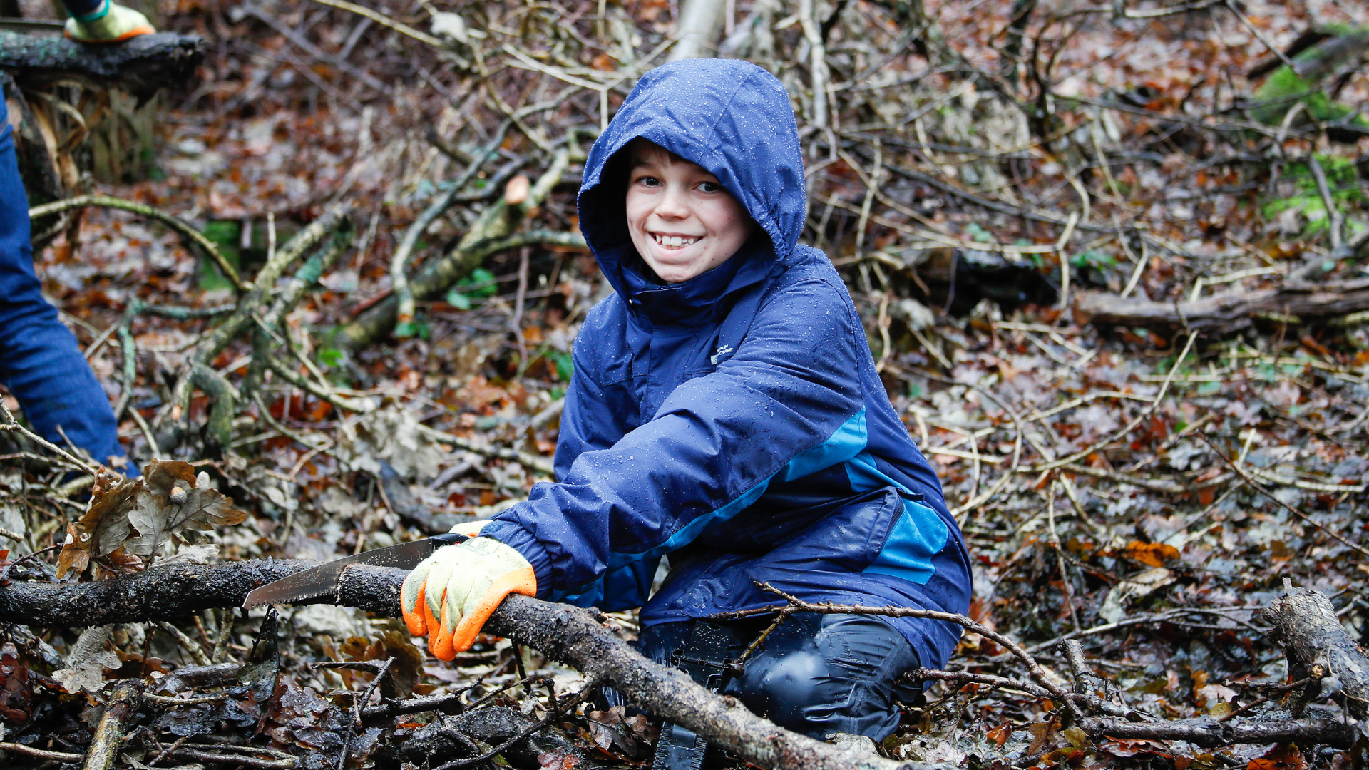 A teenage boy using tools to coppice a fallen branch in a winter Young Foresters session