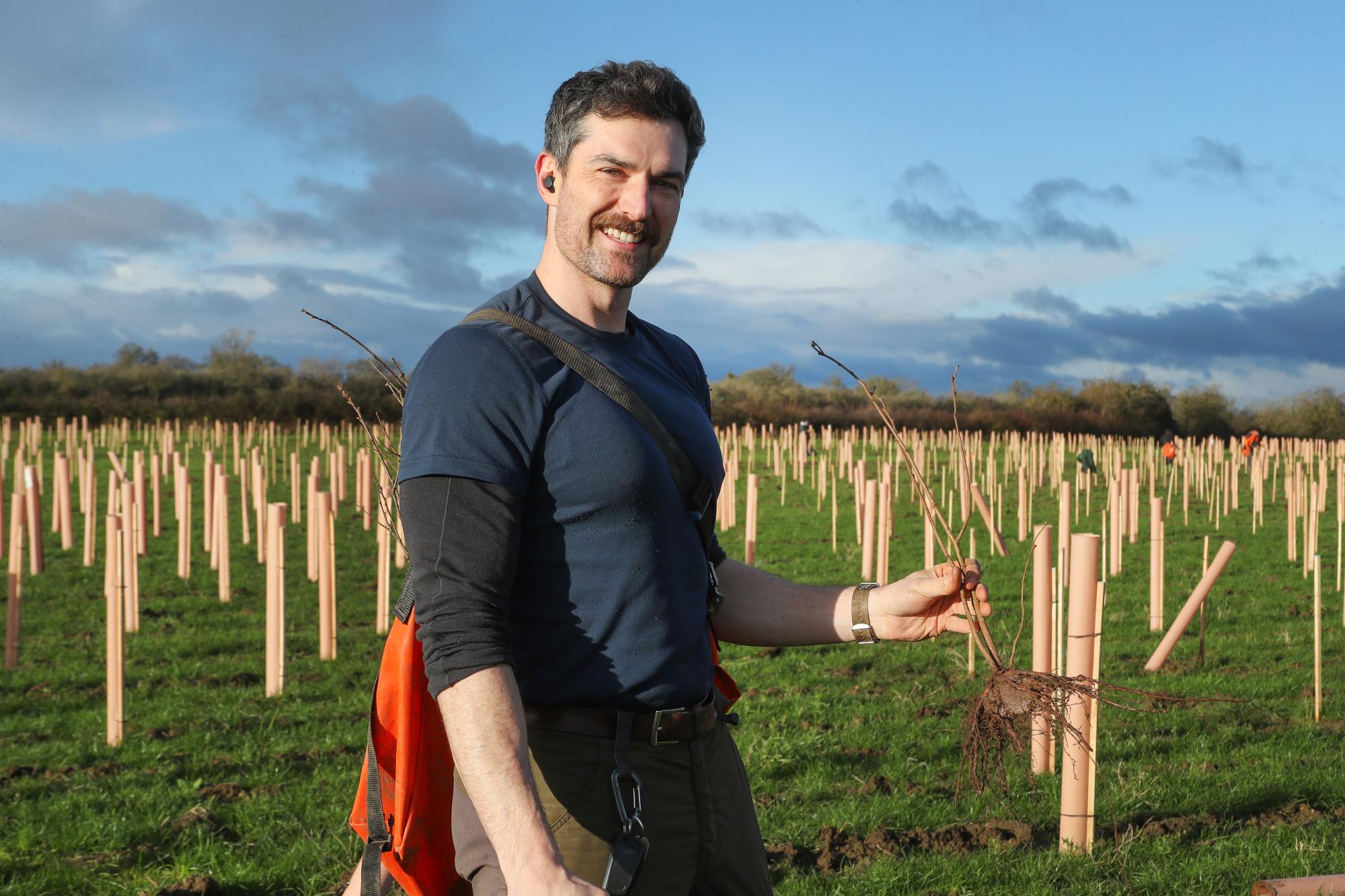 A member of the Forestry team, Fletcher Yates, smiling with saplings in tree guards in the background.