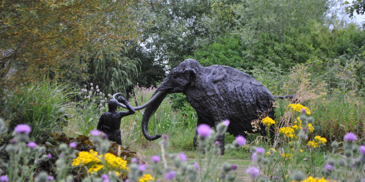 Bronze statue of a woolly mammoth surrounded by wildflowers in Garden of Heroes and Villains
