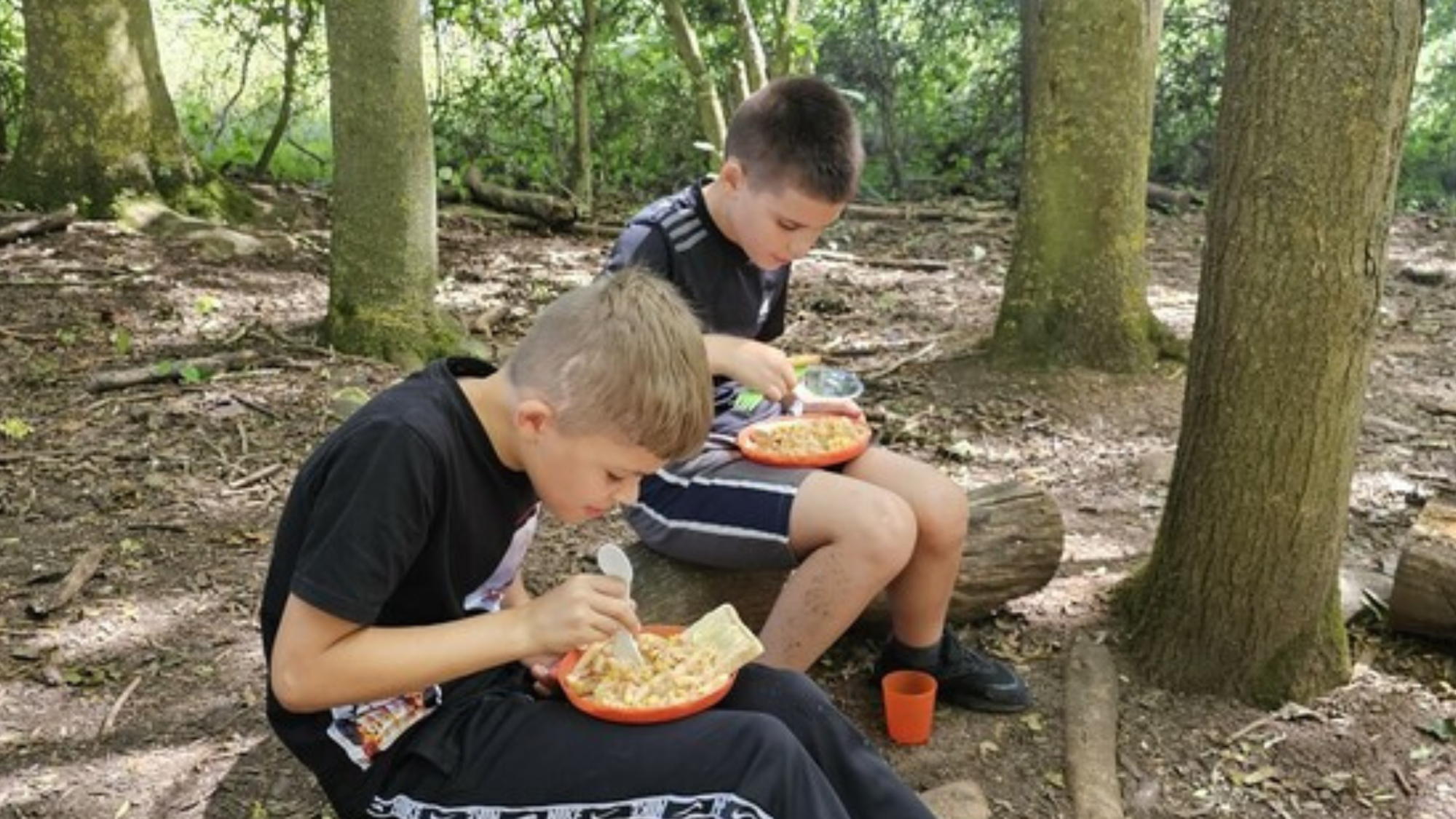 Two boys enjoying their cook in the wood meals that they carefully prepared