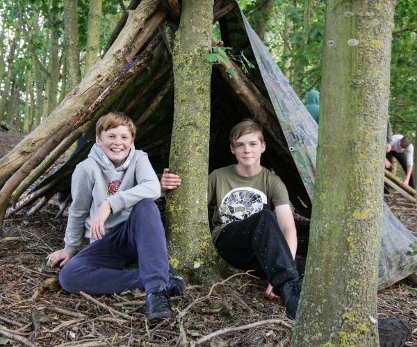 Two teenage boys sitting outside a den in the Forest