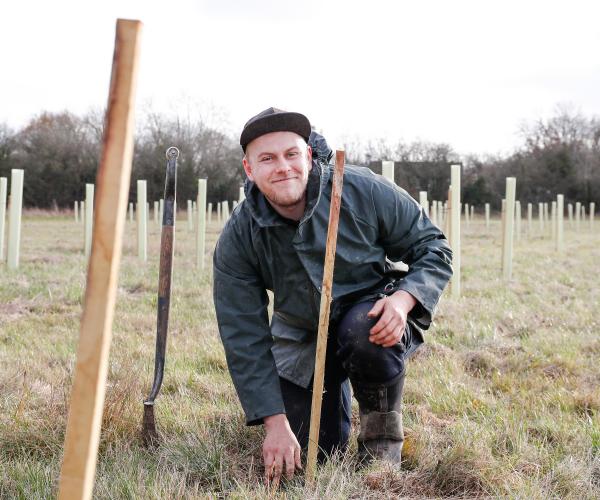 Senior Forest Ranger James crouching down smiling at the camera whilst tree planting