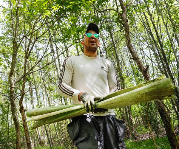Volunteer, Leon is walking through woodland with sunglasses on, he is carrying tree guards