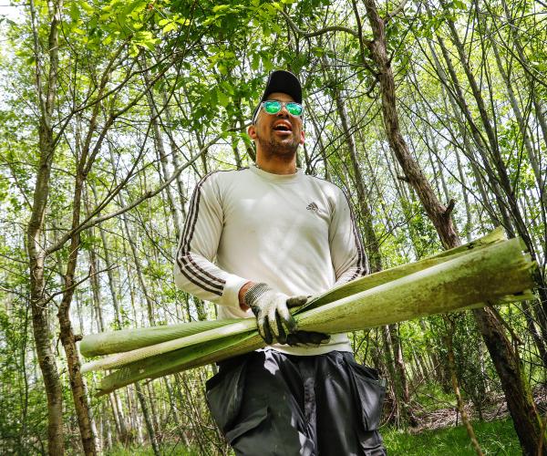 Volunteer, Leon is walking through woodland with sunglasses on, he is carrying tree guards