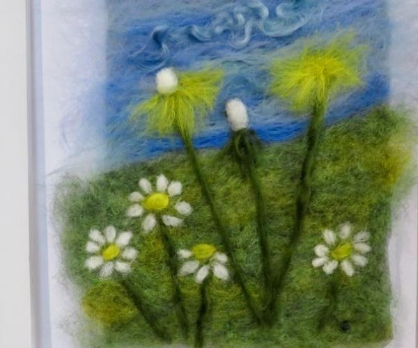 An framed felted image of flowers, grass and blue skies