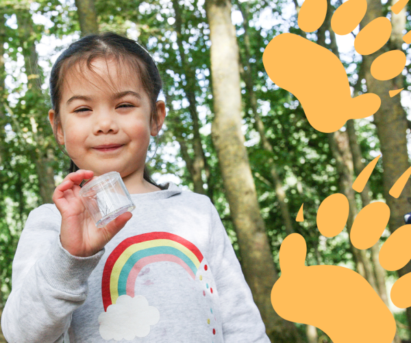 A young girl wearing a rainbow jumper holding a container. There are two orange badger tracks on the right hand side of the image.