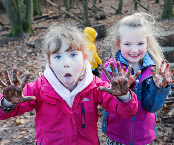 Two children showing off their muddy hands whilst having fun at Mini Foresters