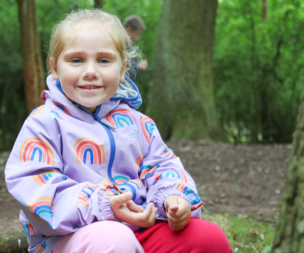 A young child smiling whilst sitting on a log in the Forest