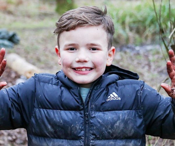 A young boy holding up his dirty hands and smiling at the camera in the Forest