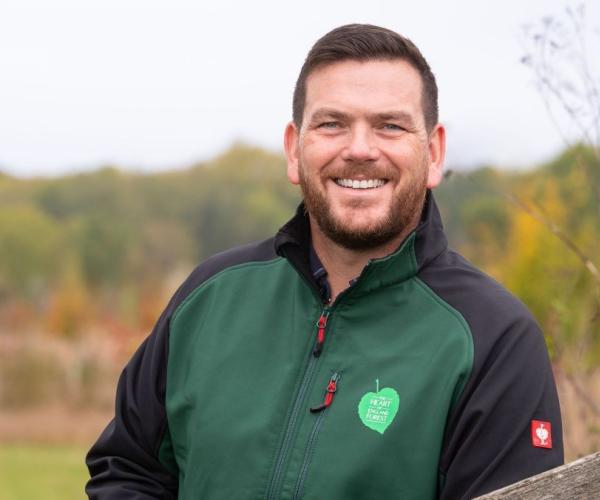 Head and shoulders shot of Andy Parsons, the charity's Chief Executive, standing by a gate with fields and trees behind him 