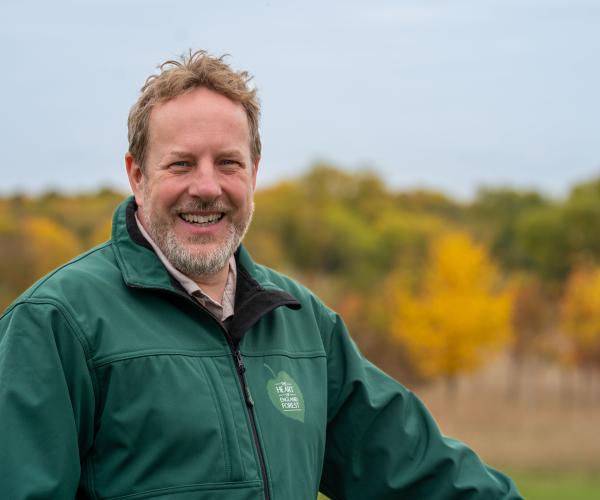 Dr David Spruce looking at the camera with the autumn trees behind him