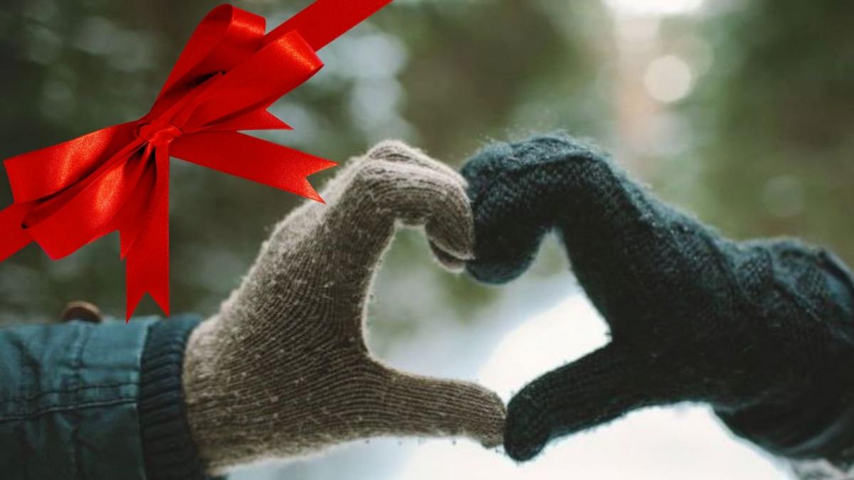 Two gloved hands forming a heart shape in front of a snowy woodland path