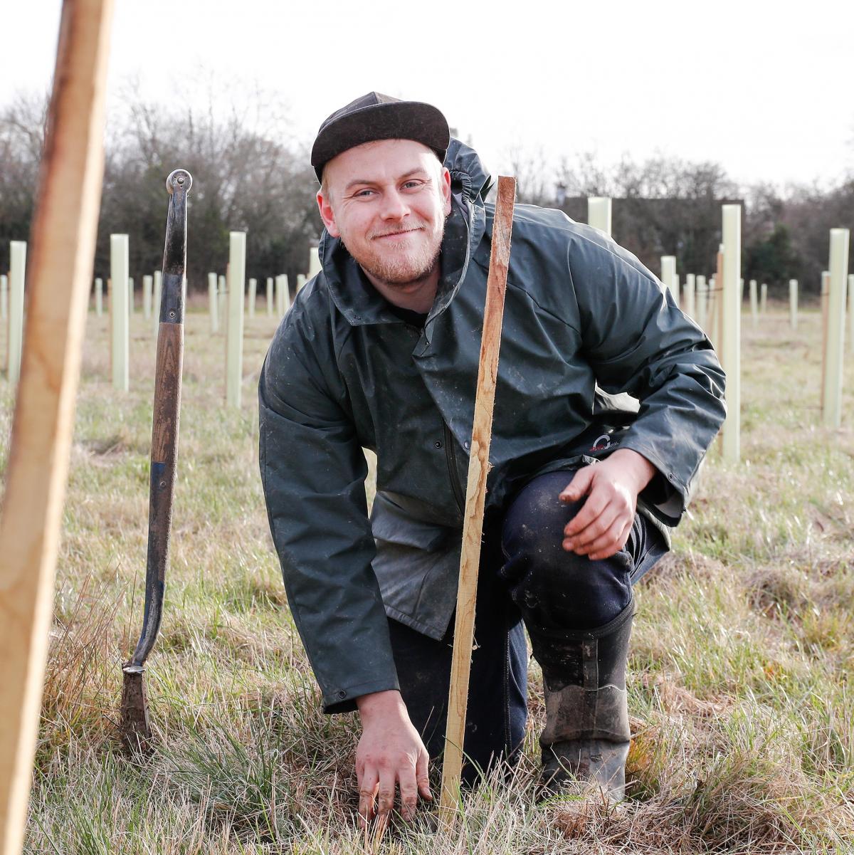 Senior Forest Ranger James crouching down smiling at the camera while tree planting