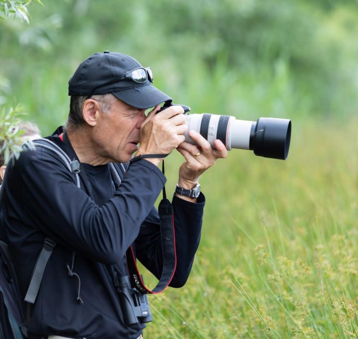 A man is holding up a long lense camera about to take a shot whilst standing in the Forest