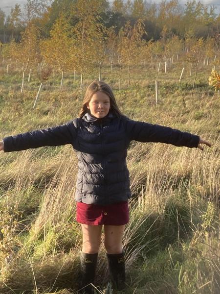 Image of 11 year old girl in wellingtons standing in front of young trees
