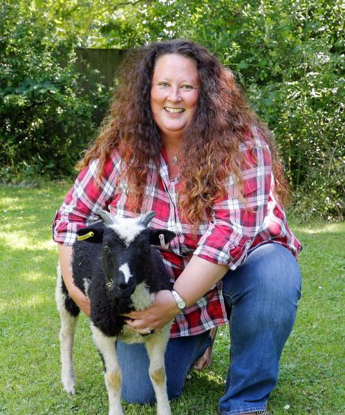 Beth Brook, Chief Executive, crouching down with a sheep next to her