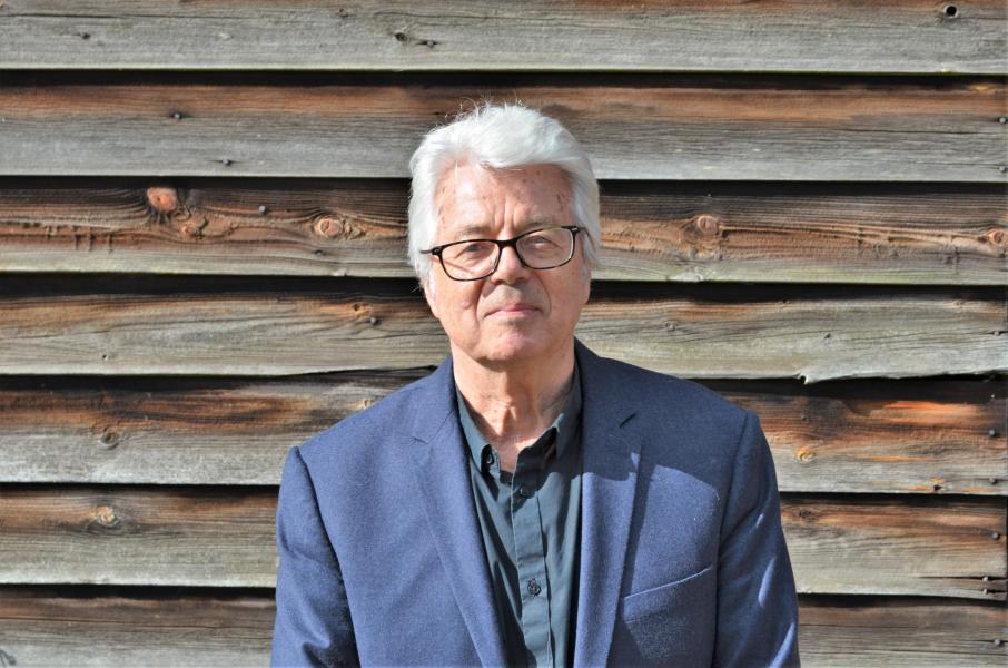 Anthony Burton in a blue suit standing in front of panelled wooden wall.