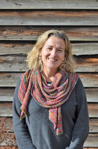 Nicky smiling in a colourful scarf in front of a wall of wooden slates.