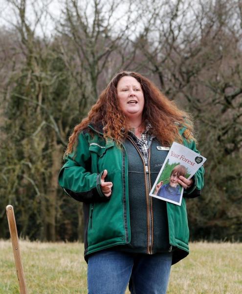 Beth Brook, Chief Executive, stood outdoors in the Forest holding a supporter magazine, speaking to people gathered at the 2 millionth tree planting 