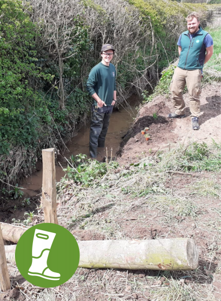 Volunteer Manager, Jonathan with Officer, Jake from the WWT standing in the creek at Arrow Mill - A graphic of a wellie in the bottom left.
