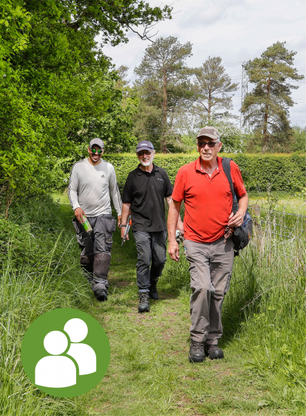 Three male volunteers walking on a freshly mown pathway toward the camera of different ages - People icon in the bottom left