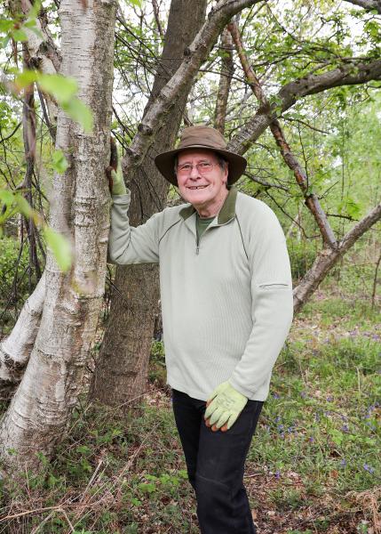 Alan Sifford, Volunteer Leader holding a tree in the Forest smiling at the camera