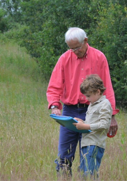 Volunteer Steve is helping a young boy identify insects. They are standing in grassland looking at a clipboard