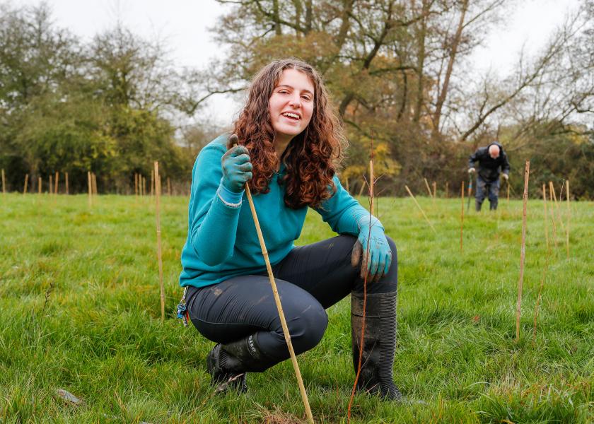 Becky, Biodiversity Intern, crouching down next and smiling next to a newly planted sapling.