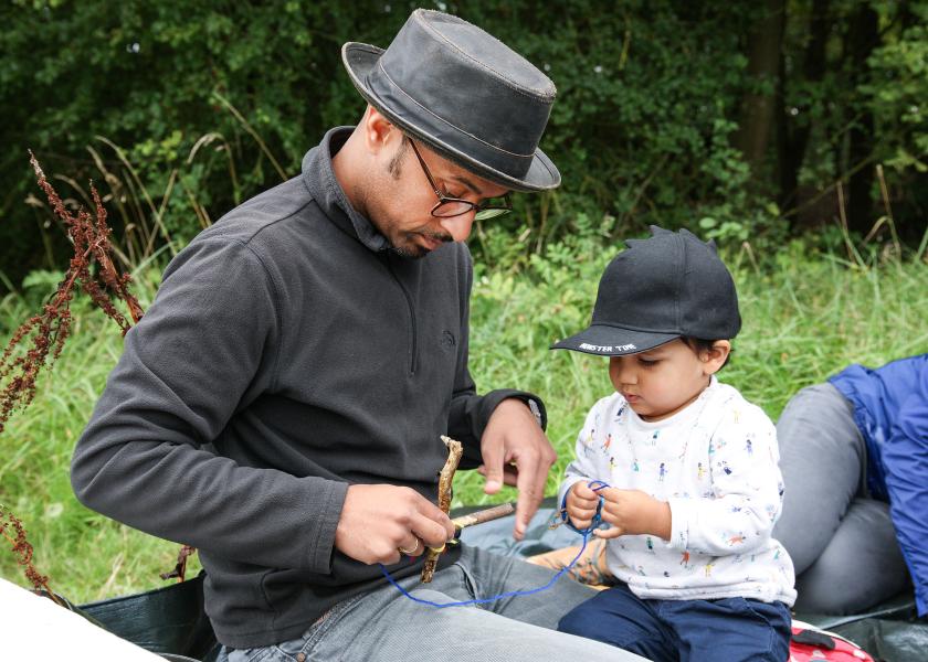A man wearing a hat and glasses with a young boy making crafts on the Forest floor