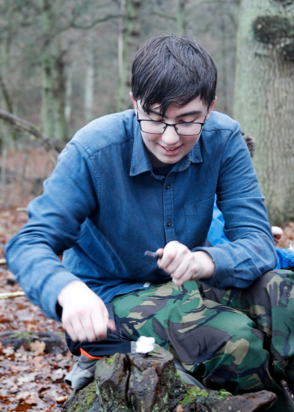 Edward crouched down smiling whilst using a hand tool on a tree strump.