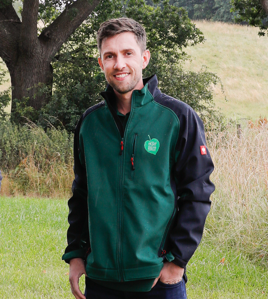 Tim stood in a field smiling with a tree in the background